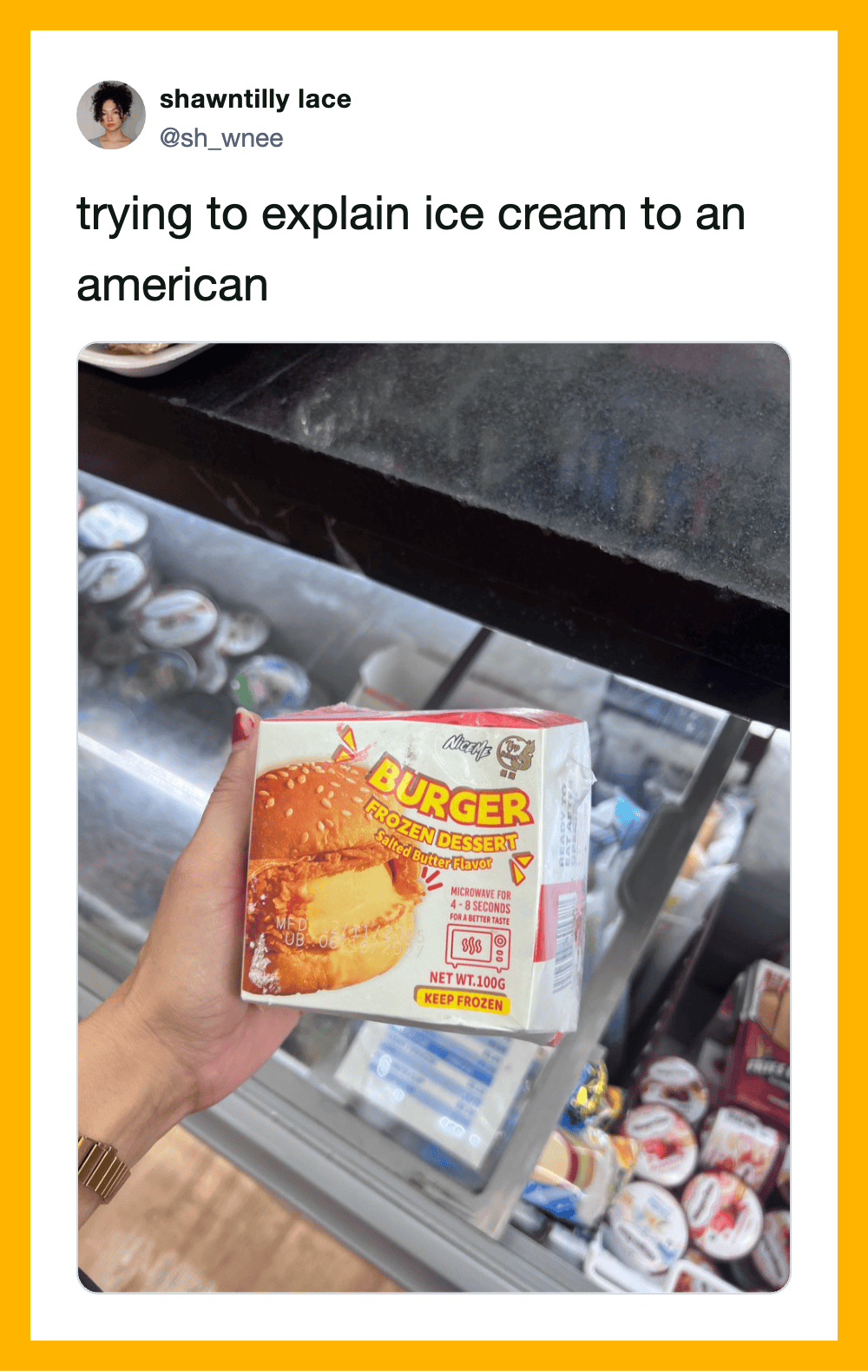 Person holding a burger-flavored ice cream box in front of a freezer filled with ice cream.