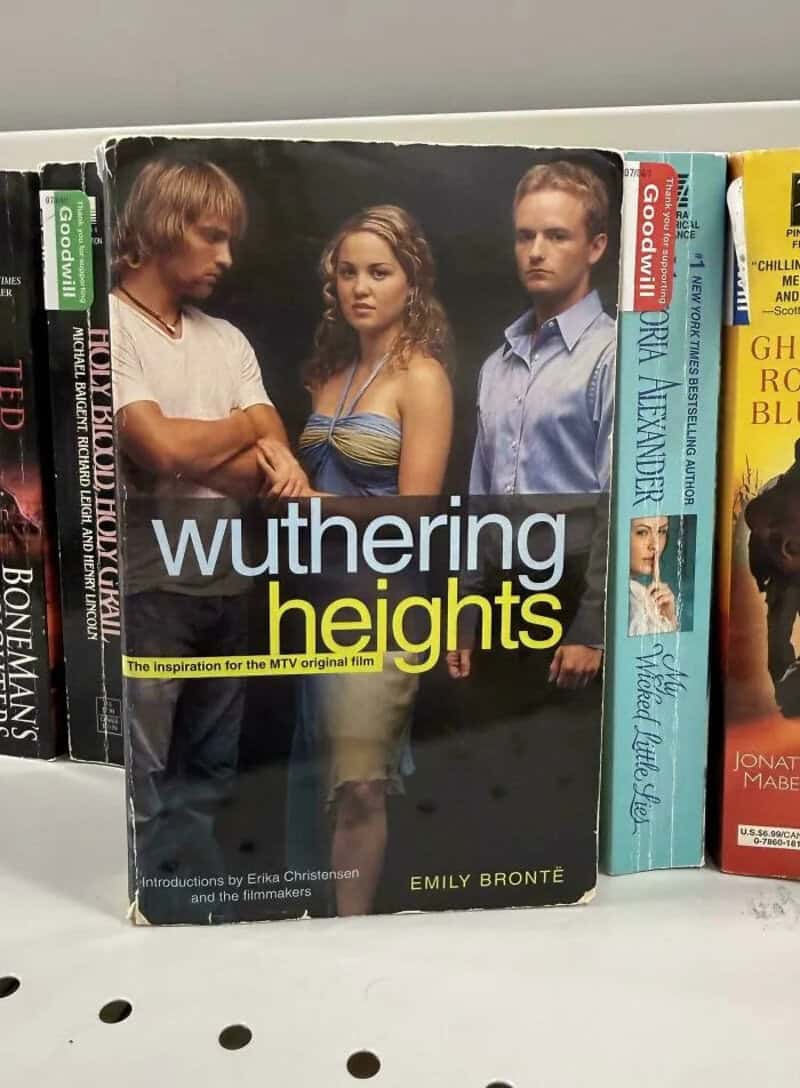 Wuthering Heights book cover with three characters, a man, woman, and another man, on a bookshelf.