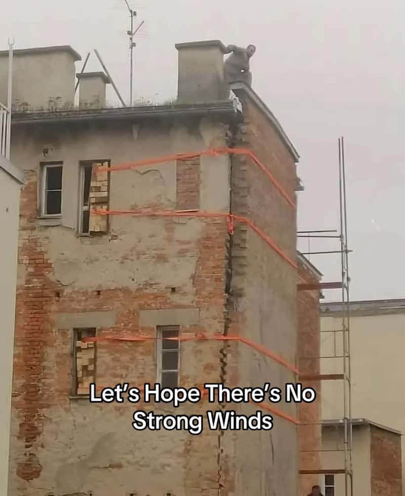Worker on roof with scaffolding, orange safety lines, and a message about wind.