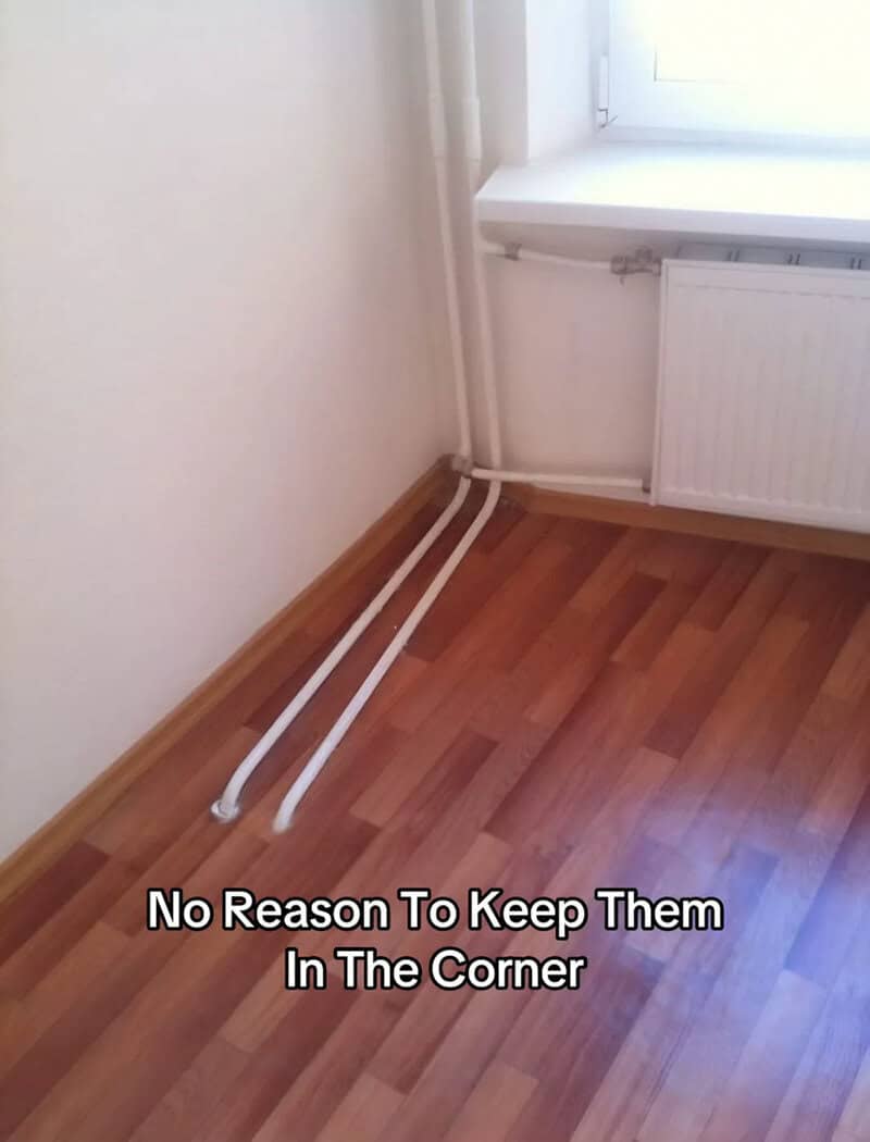 Pipes run along the corner of a room near a radiator and window.