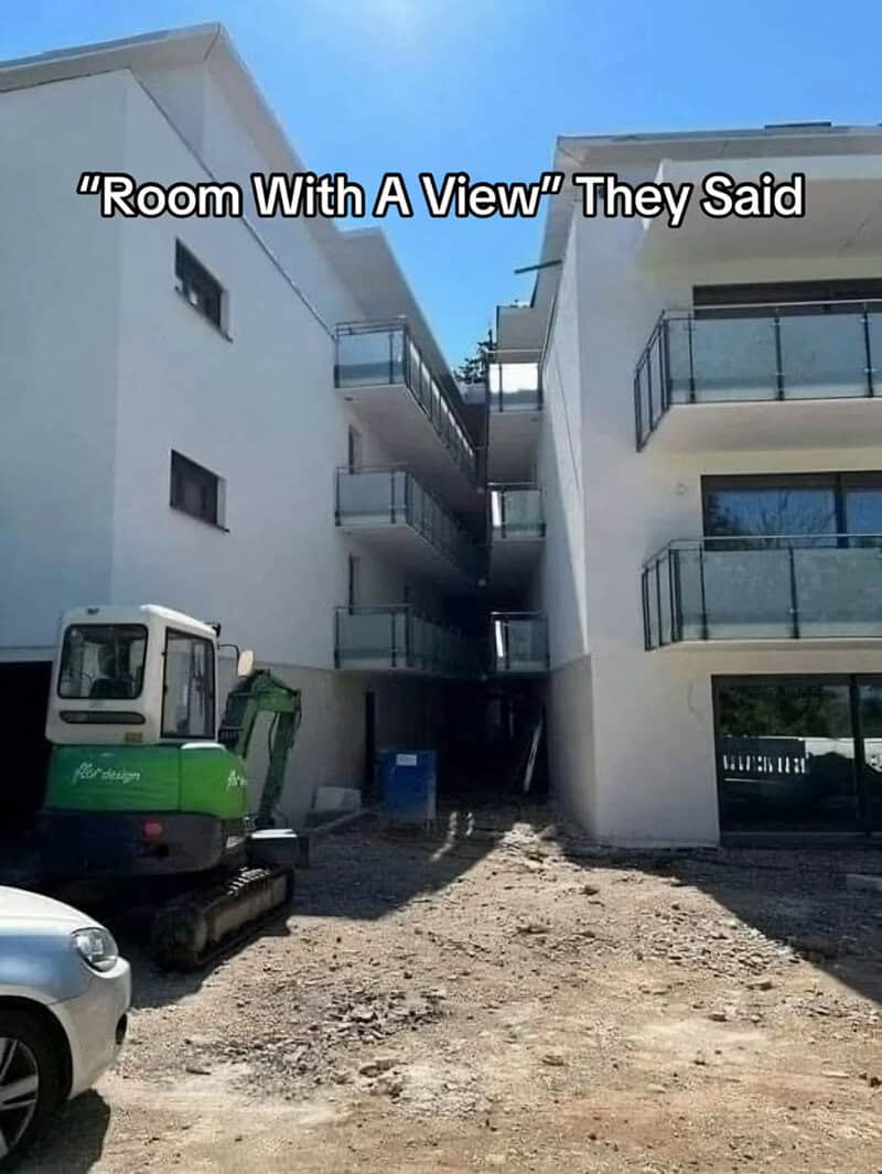 Construction site between two white buildings with balconies, captioned "Room With A View" They Said.