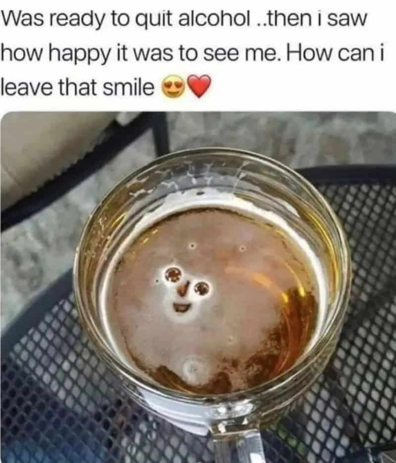 A glass of beer with a face-like pattern on the foam surface.