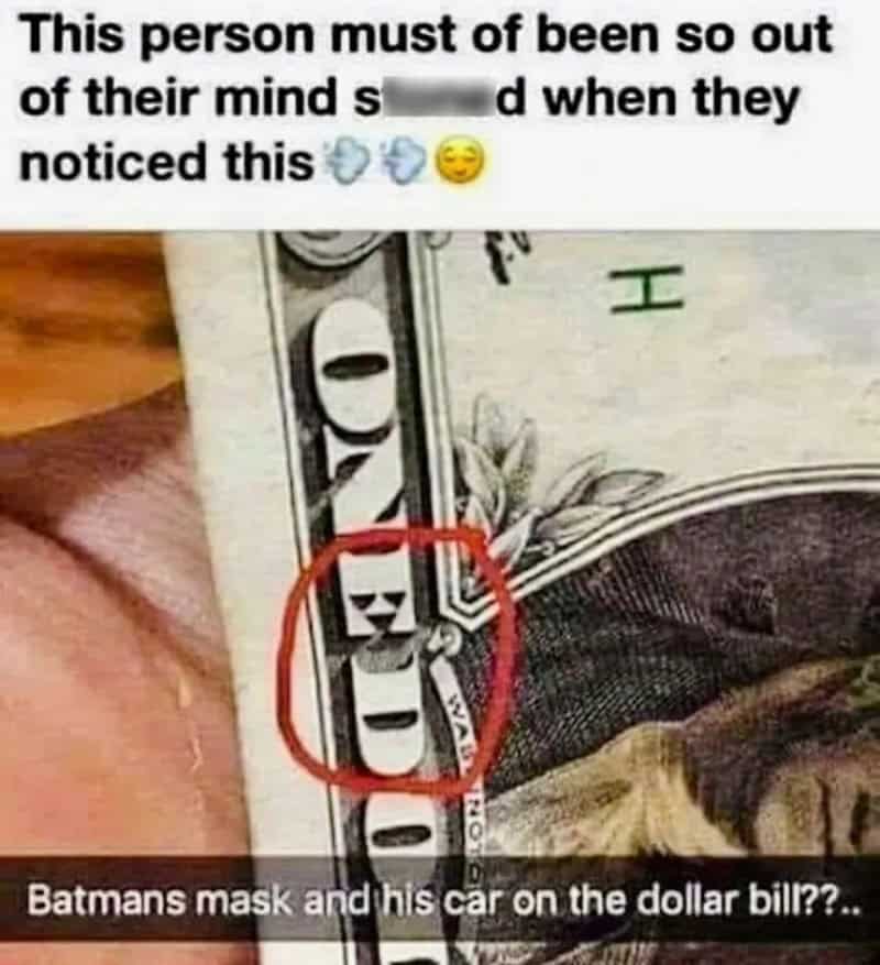 Person's hand holding a dollar bill with Batman's mask visible on the bill.