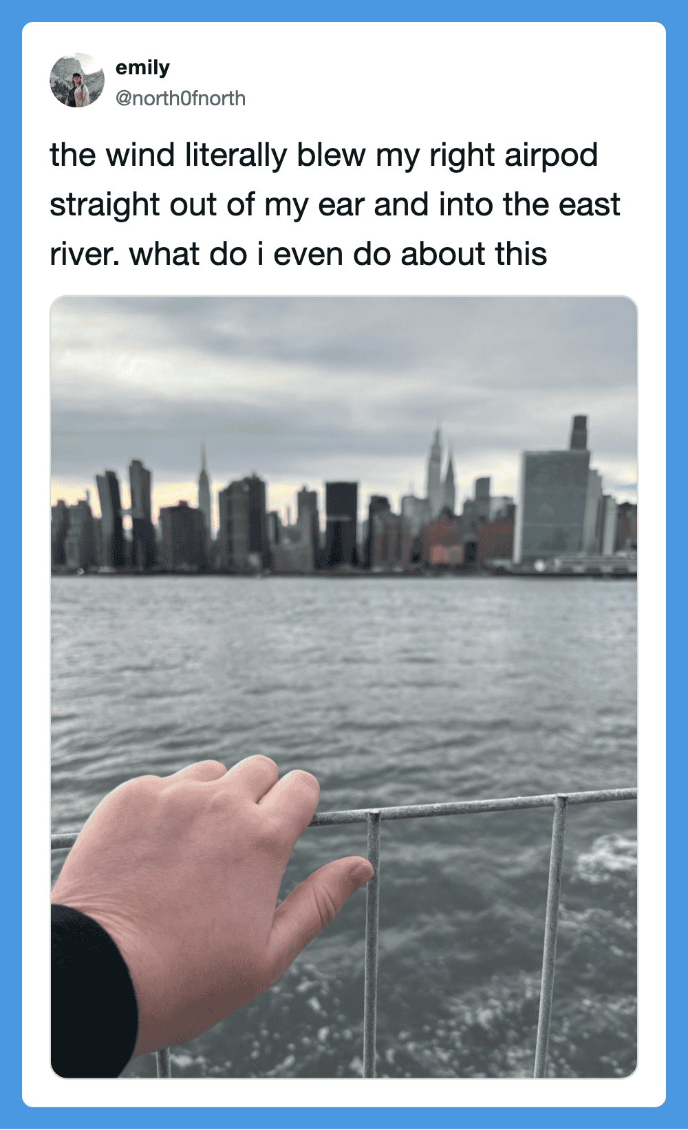 Hand holding onto a railing with New York City skyline in the background during windy weather.