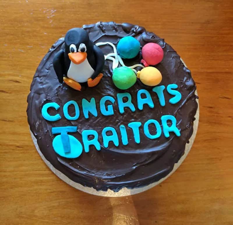 Chocolate cake with a penguin figure and colorful balls, says 'Congrats Traitor'.
