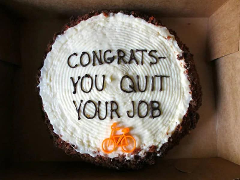 Cake with 'CONGRATS YOU QUIT YOUR JOB' written on it and a small orange bicycle decoration.