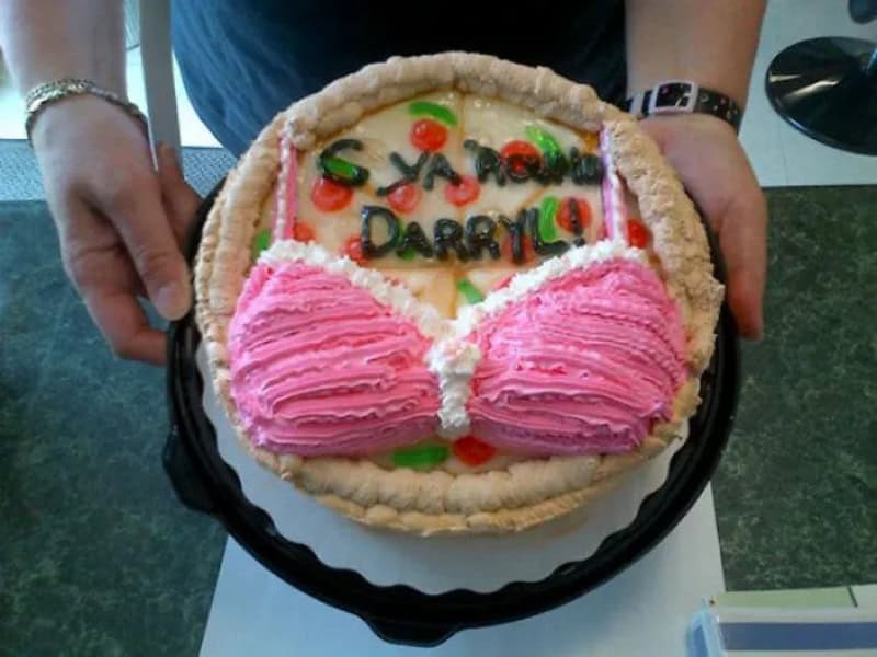 Cake with a message and pink frosting bra design, held by two hands.