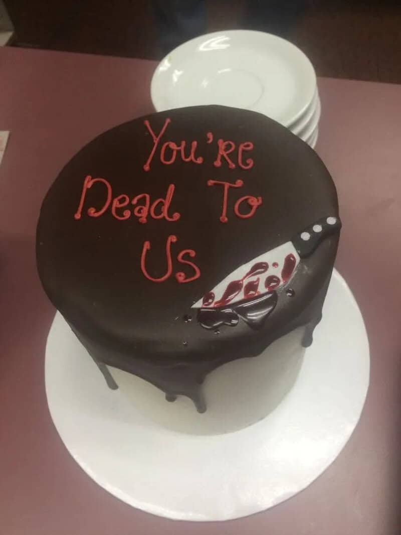 Cake with black icing and red writing: You're Dead To Us, with a knife decoration.