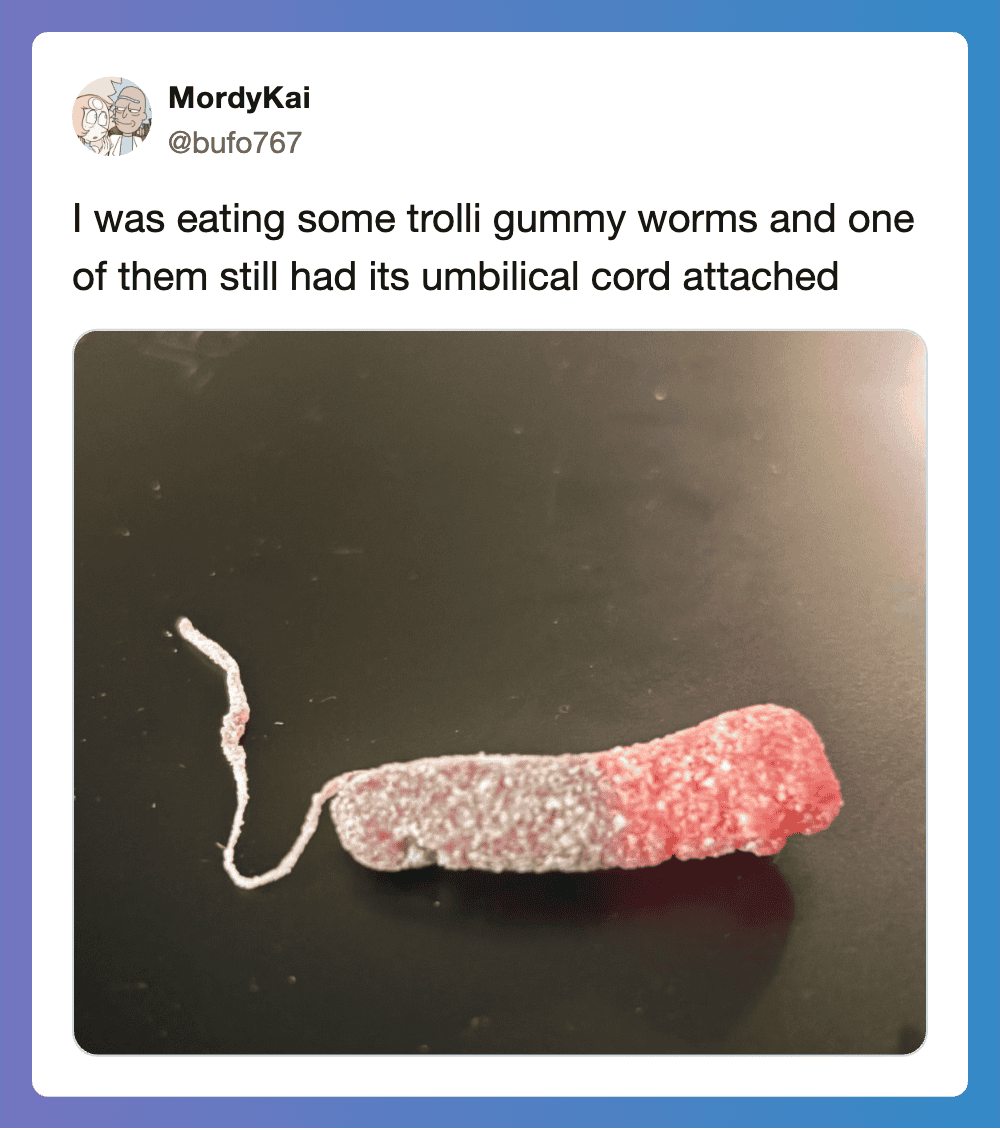 A gummy worm with an umbilical cord attached, lying on a black surface.