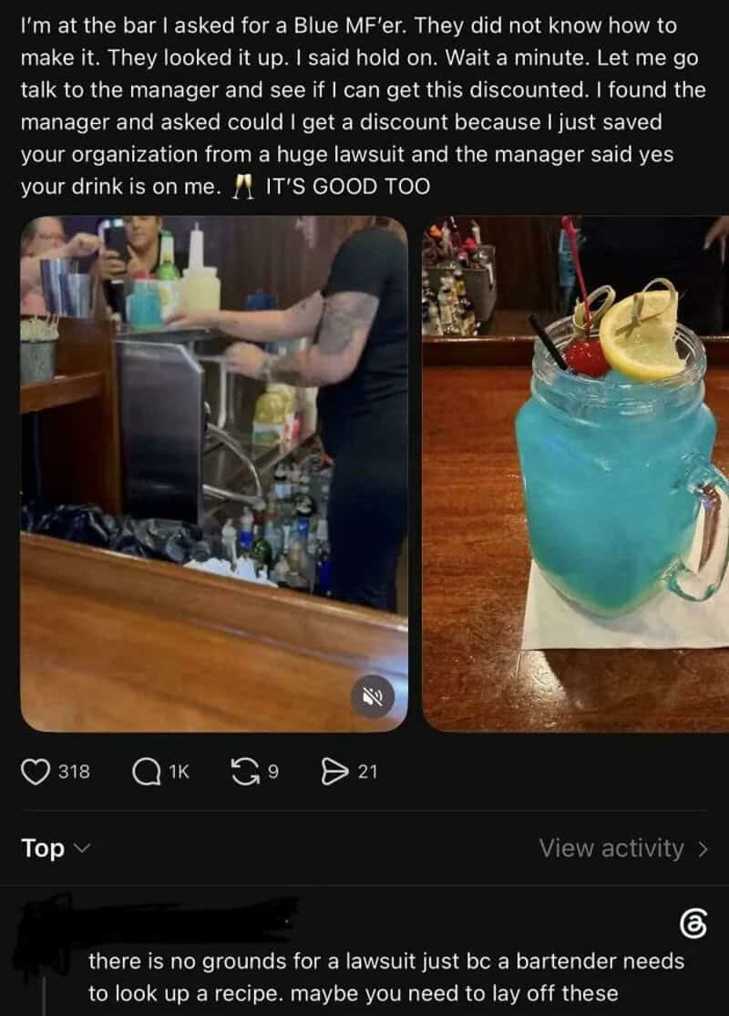 Barista serving a blue cocktail with lemon and cherry garnish at a bar.