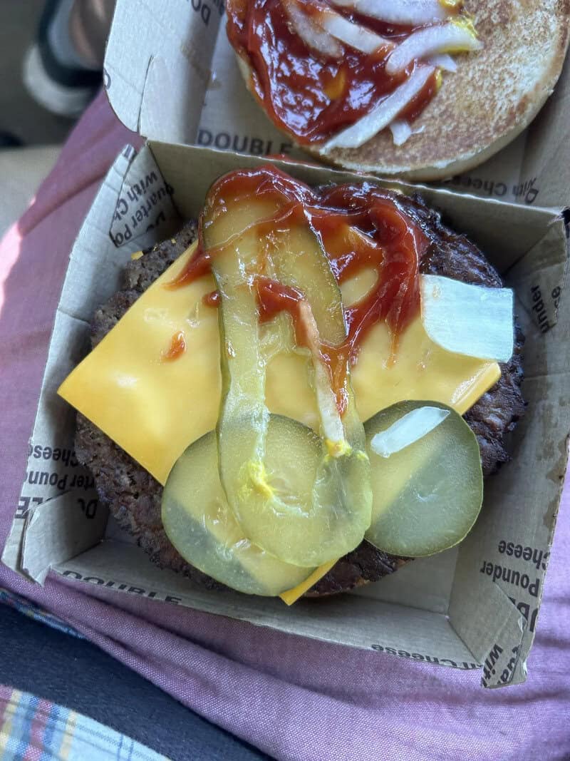 A burger with pickles, cheese, onions, ketchup, and mustard in a paper container.