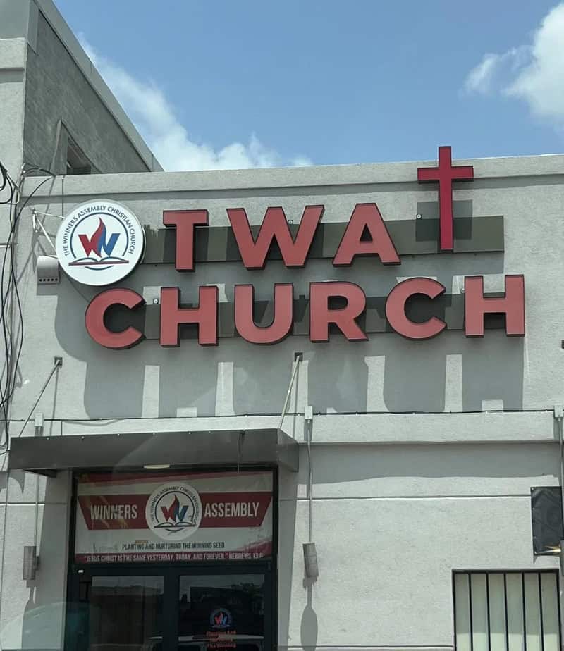 TWA Church sign with a cross on top and a logo with a dove and Bible.