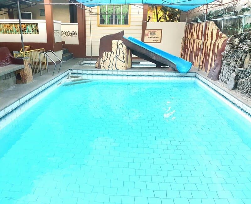 Empty swimming pool with a blue slide and rock decorations, under a blue canopy.