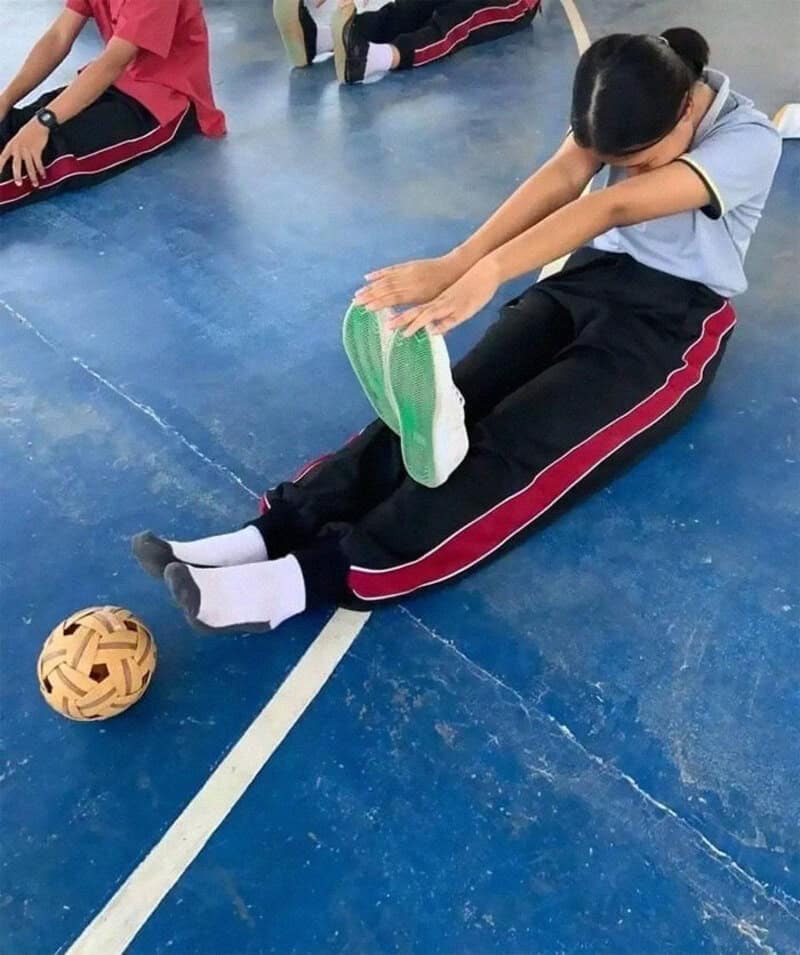 Girl stretching on the floor with a ball nearby in a gym class.