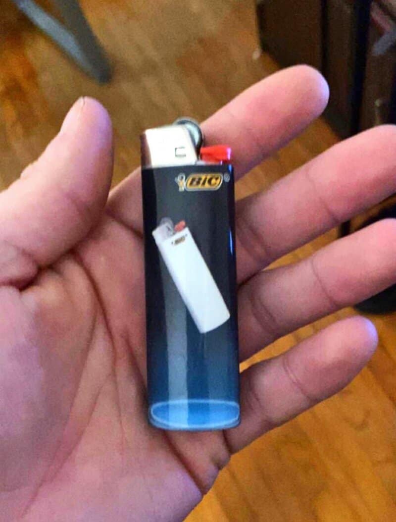 Hand holding a BIC lighter with a blue transparent body and red ignition button.