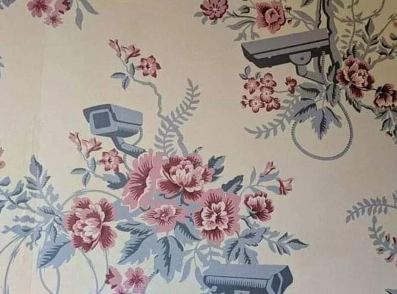 Security cameras and a gun on floral wallpaper wall.