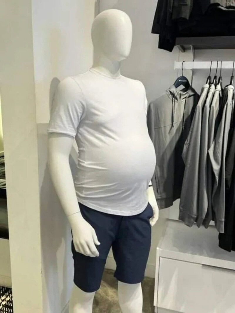 Mannequin with a pregnant belly wearing a white t-shirt and navy shorts in a clothing store.