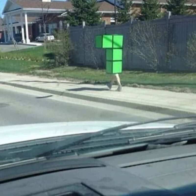 Person dressed as a Tetris block walking on sidewalk near street.
