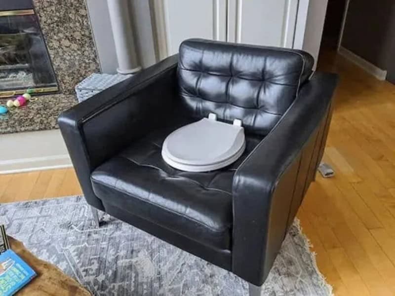 Black leather armchair with a white toilet seat on top, in a living room.