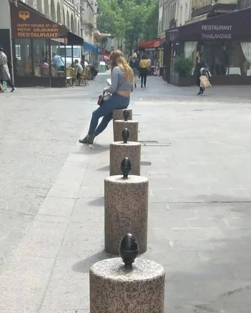 Woman sitting on a bench with a row of bollards in front of her.