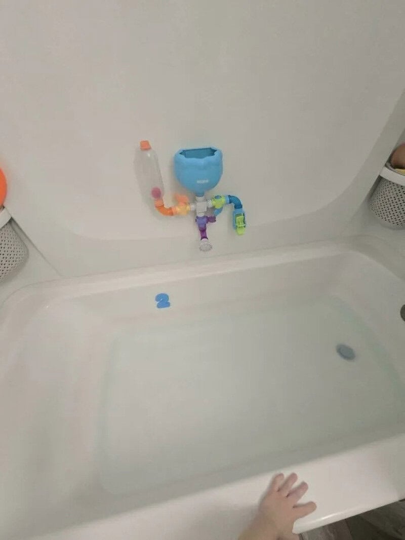 Child's hand reaching into a bathtub with a toy faucet and water container attached to the wall.