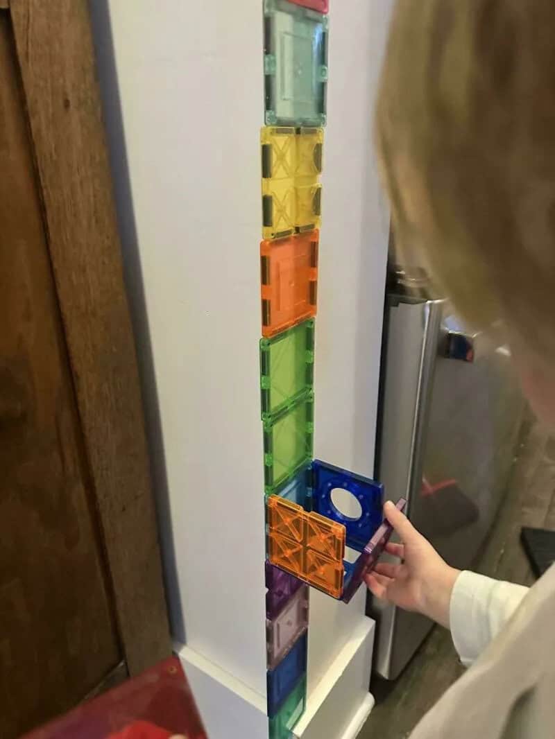 Child stacking colorful plastic containers on a white shelf.