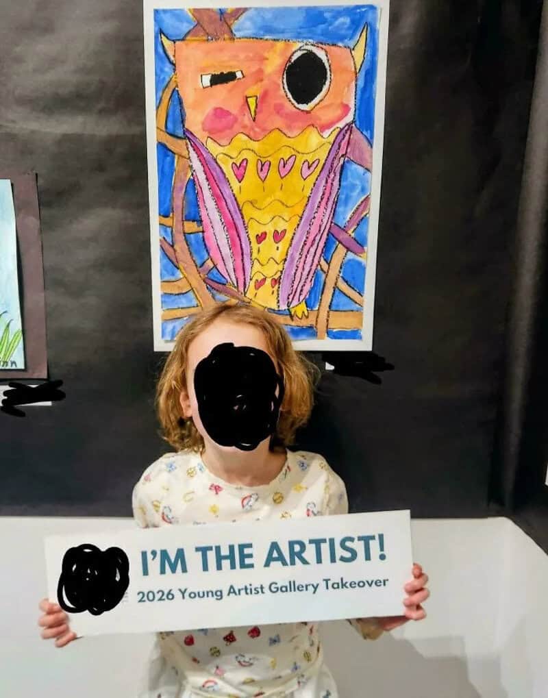 Child holding a sign in front of a colorful owl painting at the Young Artist Gallery.