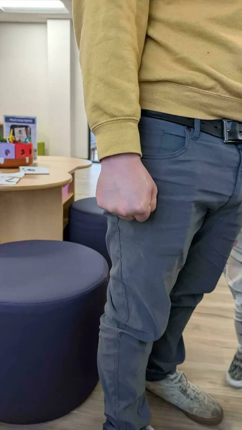 Close-up of a man in a yellow sweatshirt and gray pants with a clenched fist.
