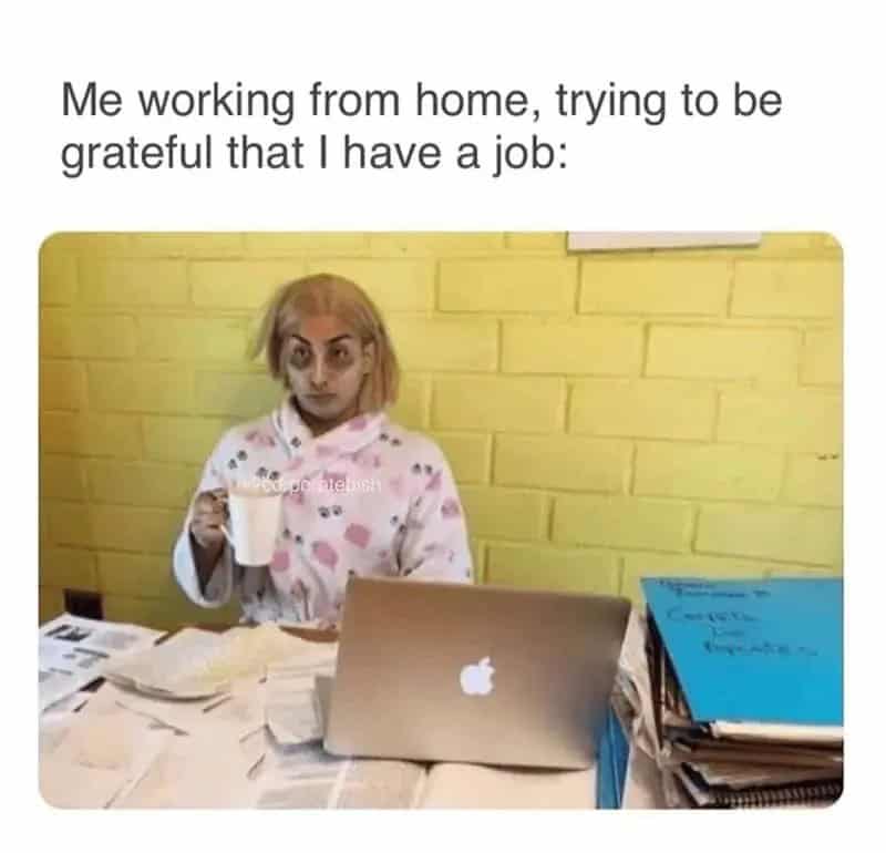 Person working from home with a laptop and coffee, looking tired.