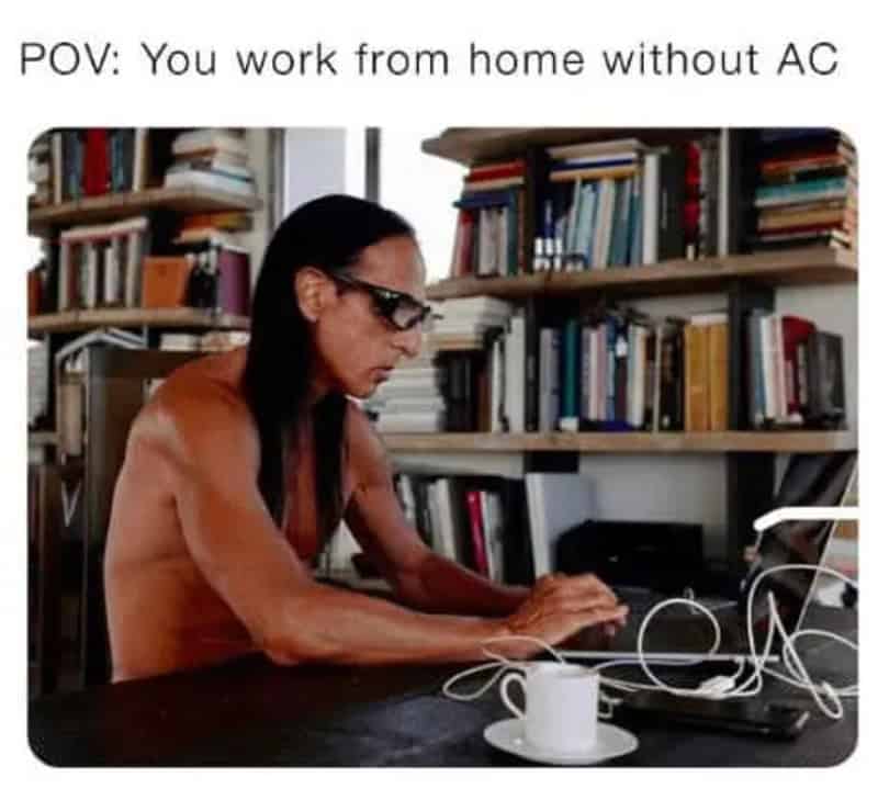 Woman working at home without AC, using a laptop, with bookshelves in background.