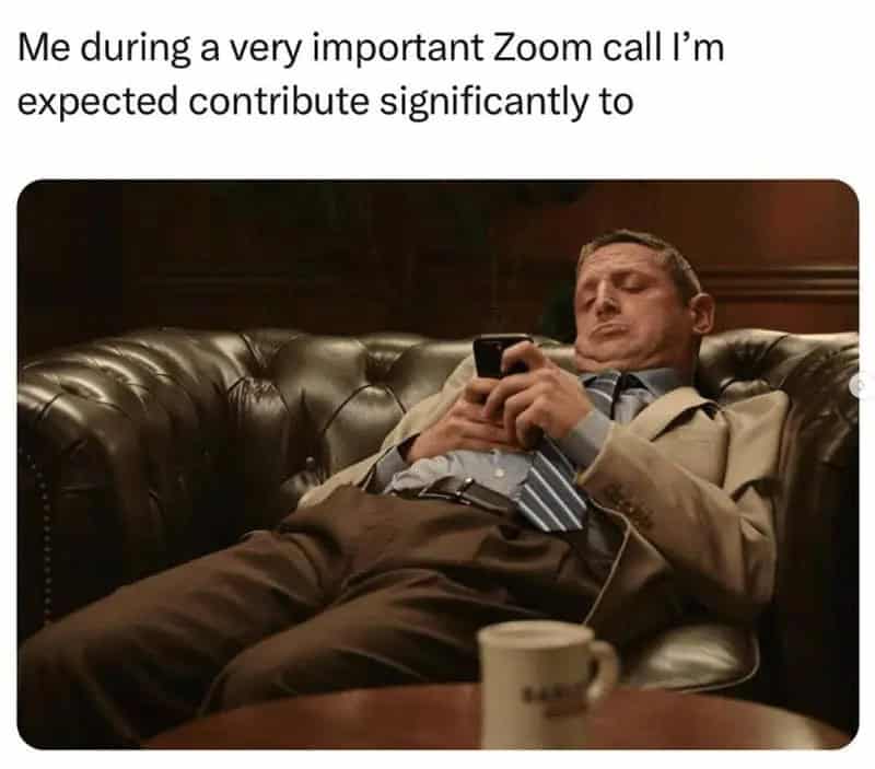 Man in suit lying on leather sofa, using phone during Zoom call.