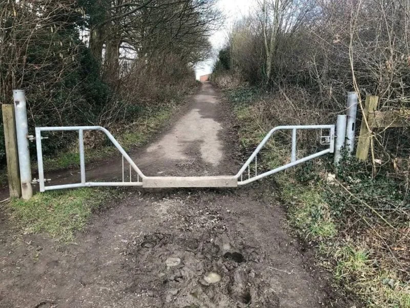 A metal gate blocking a dirt path through a wooded area.