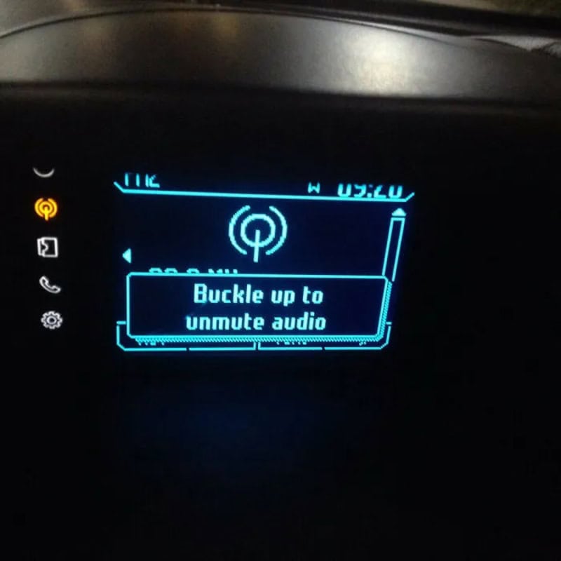 Car dashboard screen with a message to buckle up to unmute audio.