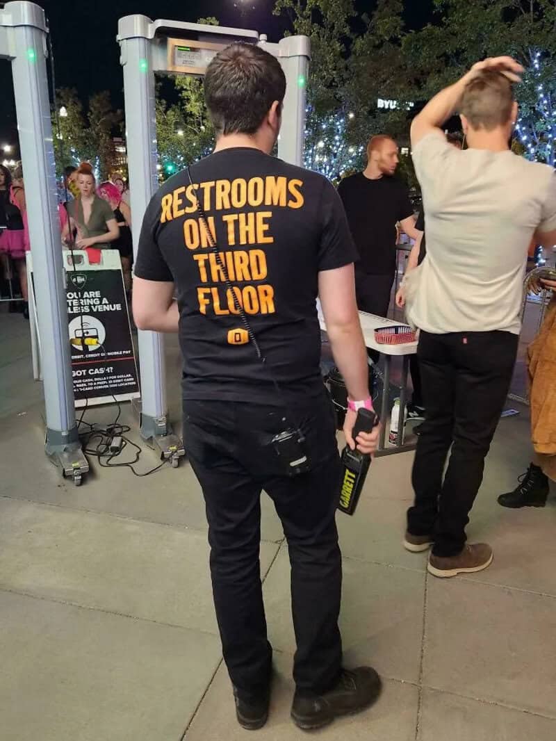 Person wearing a black T-shirt with orange text at an outdoor event.