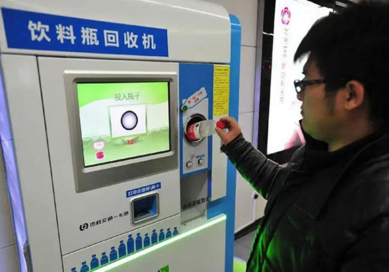 Person using a drink bottle recycling machine with a screen and coin slot.