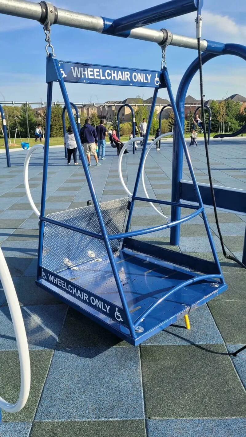 Blue wheelchair swing with 'WHEELCHAIR ONLY' signs at a playground.