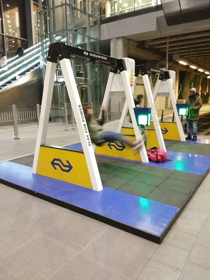 Swinging seats with a yellow and blue base in a public space.