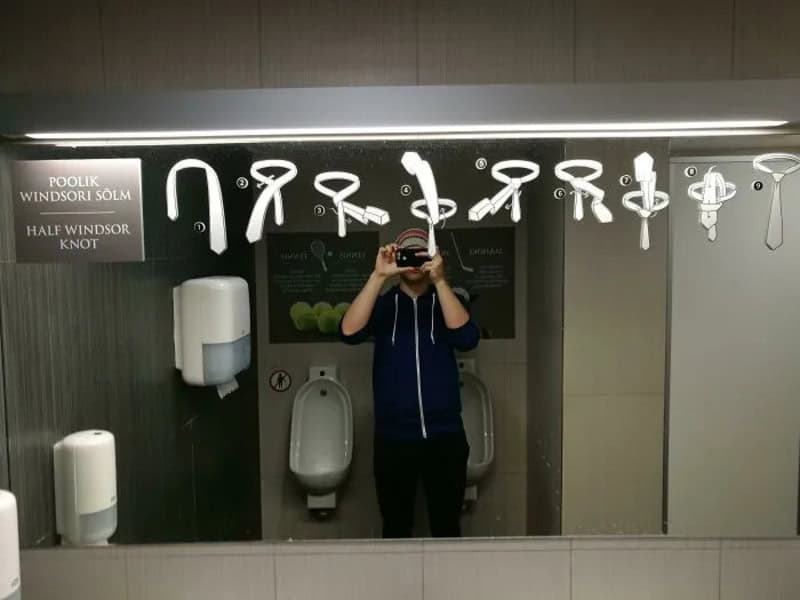 Mirror with various hooks and tools for tying knots, with a person taking a photo.