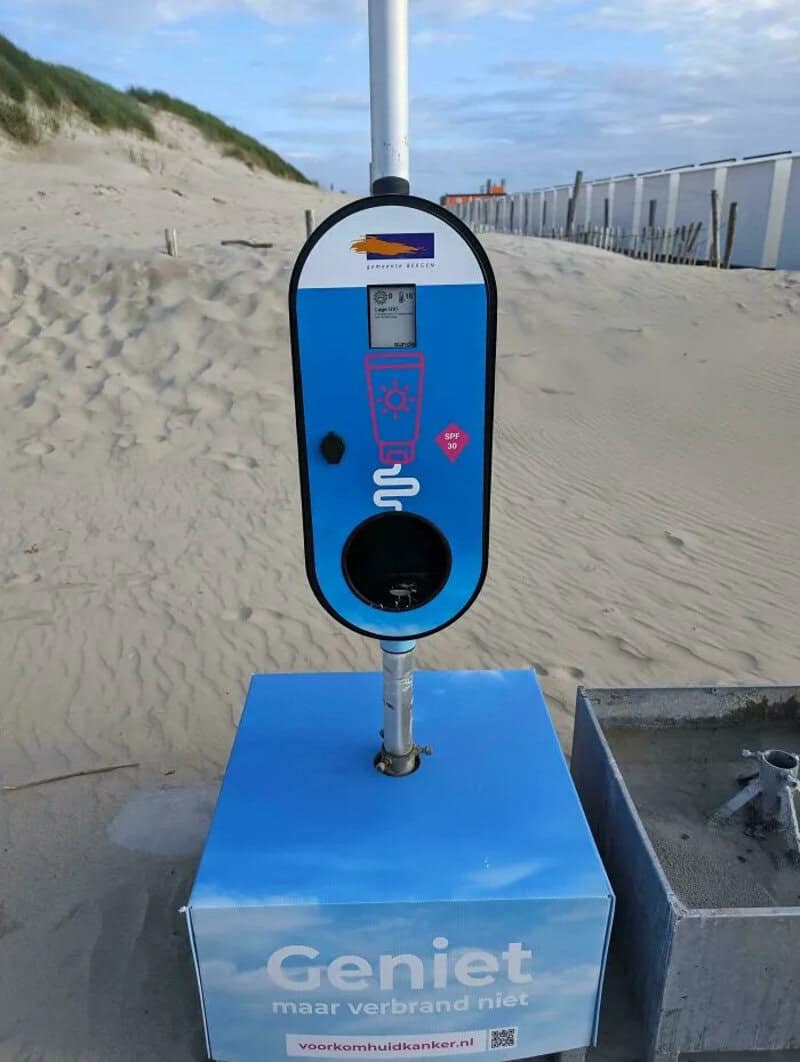 Electric vehicle charging station on the beach with a sign that says 'Geniet maar verbrand niet'.