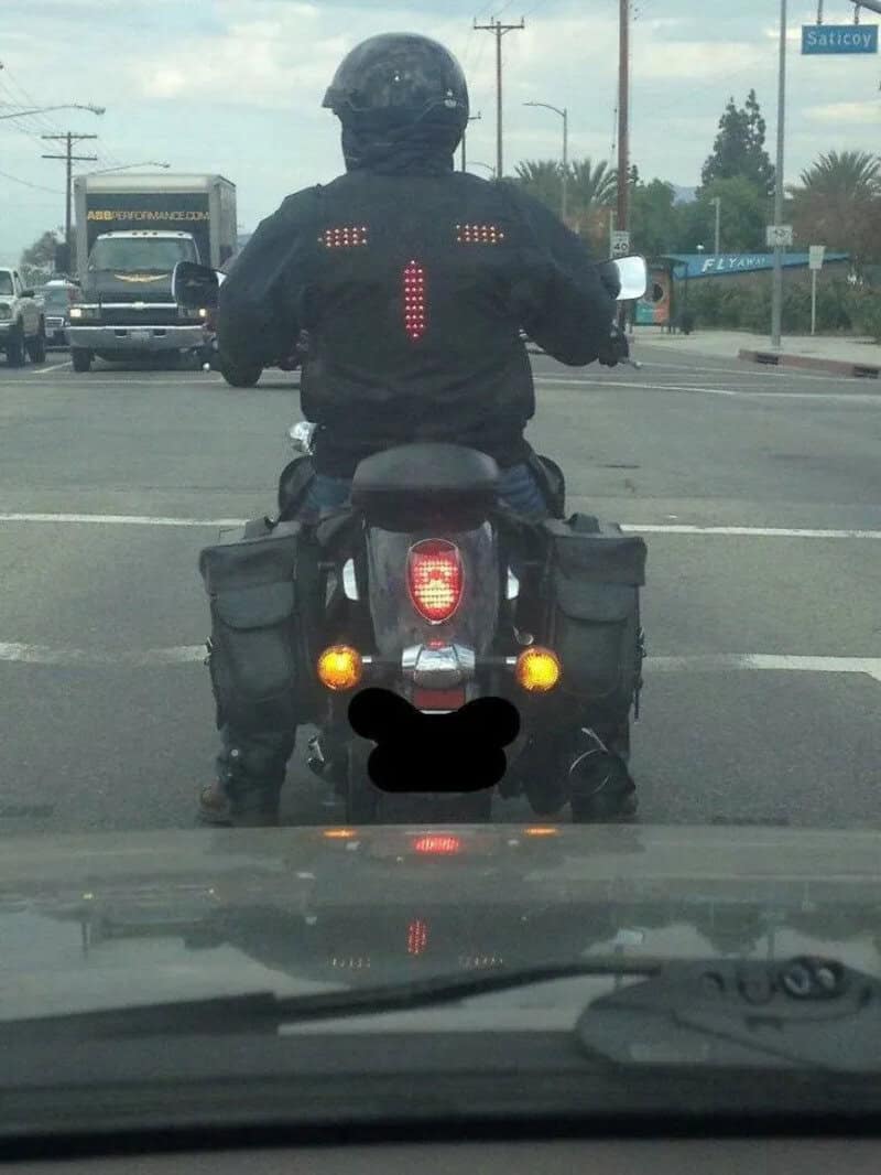 Motorcycle rider with a red LED arrow sign on back, indicating a turn.