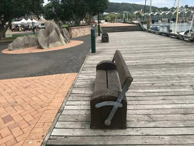 A wooden bench on a dock with a view of boats and water in the background.