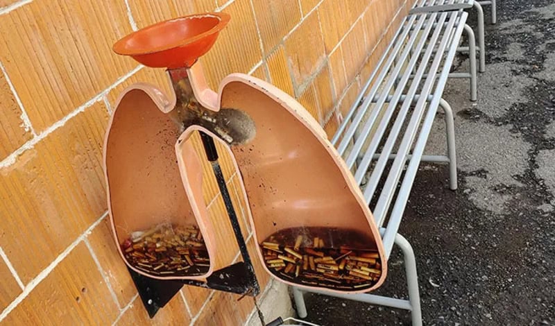 A broken outdoor water fountain with a bowl on top and two basins below, one filled with dirty water.