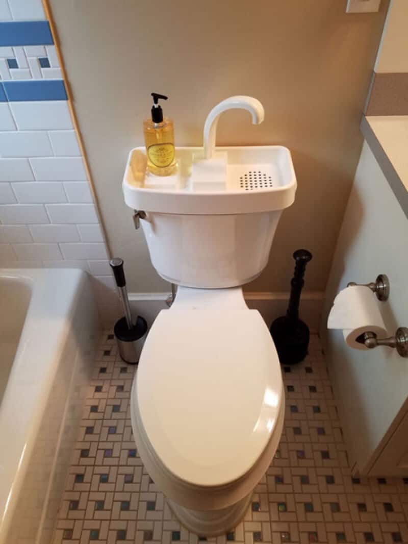 Toilet with sink on top, soap dispenser, and toilet brush in a small bathroom.