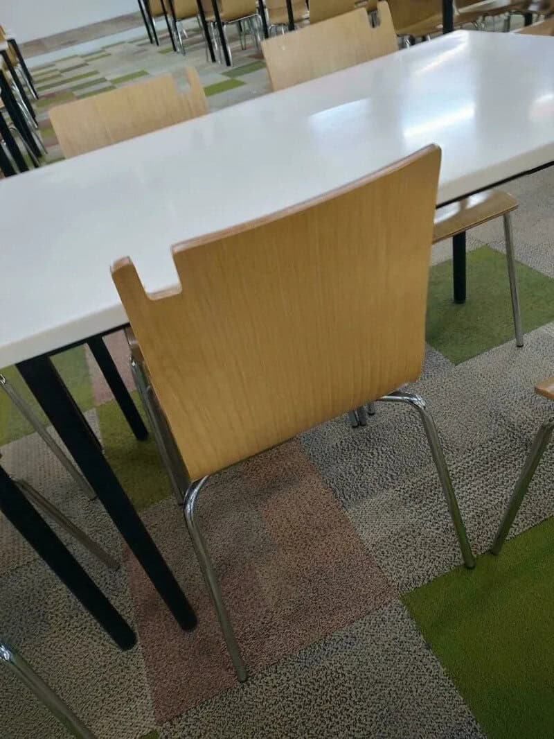 Chair with a cutout on the backrest at a white table in a cafeteria.