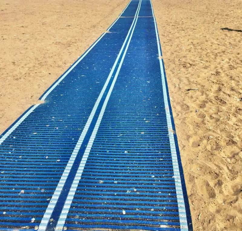 Blue solar panel walkway on sandy beach with white lines and small white dots.