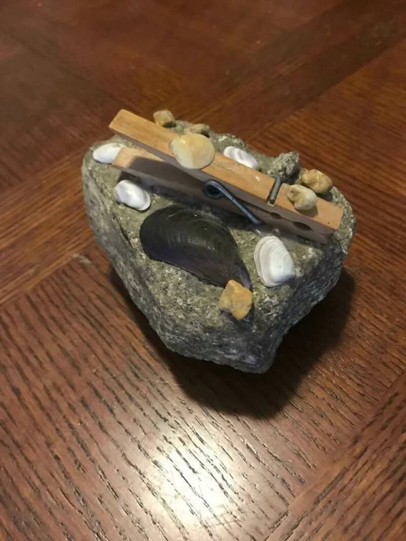 A small rock with a wooden clothespin and tiny stones on top, placed on a wooden surface.
