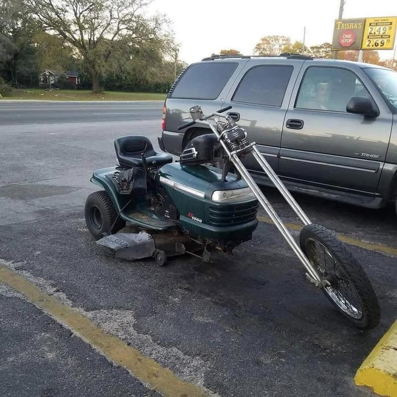 A motorized scooter with a motorcycle front wheel attached, parked in a lot.