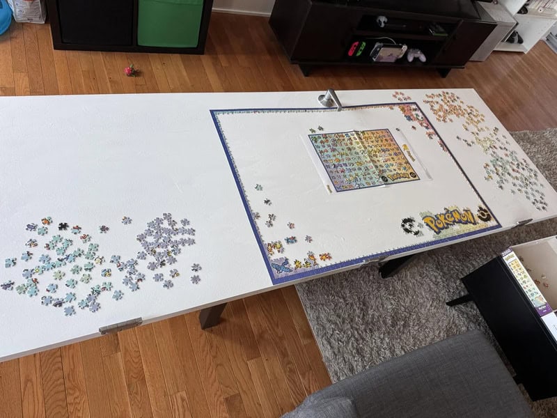 Table with scattered puzzle pieces and a nearly completed Pokémon puzzle.