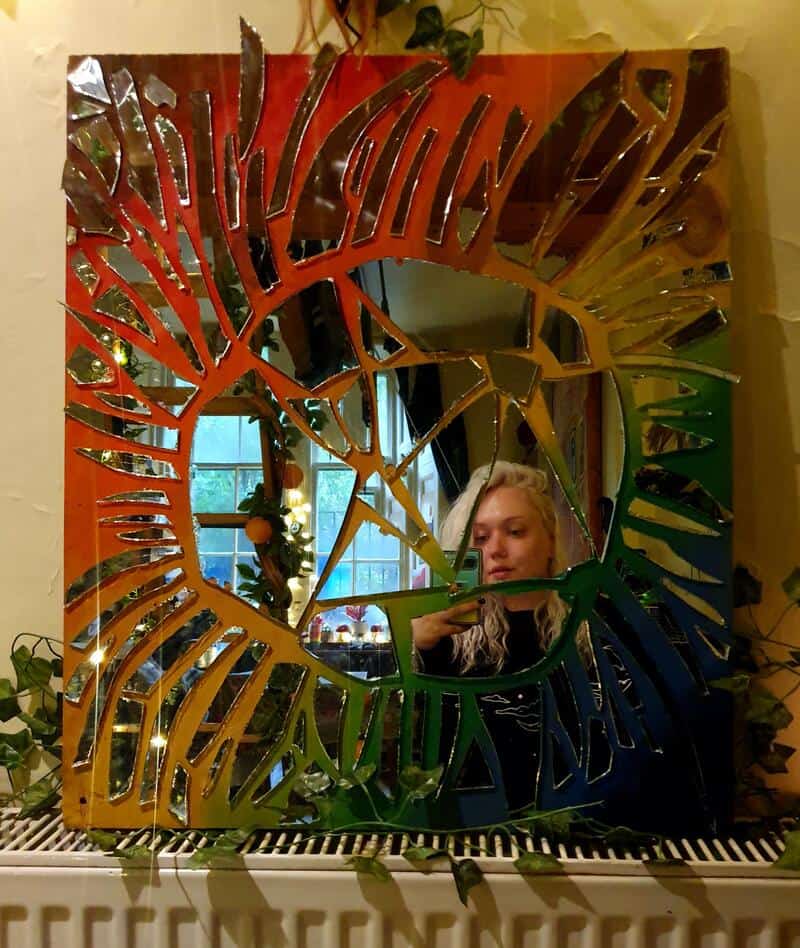 Colorful mirror with a sunburst design and a woman taking a photo in it.