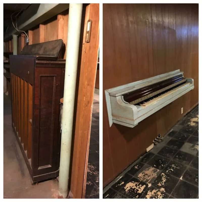 Old upright piano with damaged keys and worn finish, against a wooden wall.